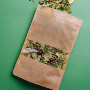 Leaf tea spilled out of a paper packet with orange slices on green background